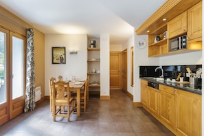 Una cocina con armarios de madera, una mesa de comedor con sillas y un ventanal con cortinas.