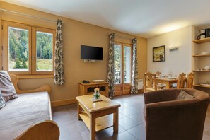 Una habitación con una cama, una mesa de madera, un sillón marrón, un televisor y un comedor con sillas y una mesa.
