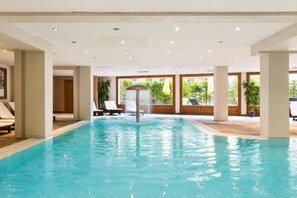 En inomhuspool med klart vatten, omgiven av solstolar och krukväxter.