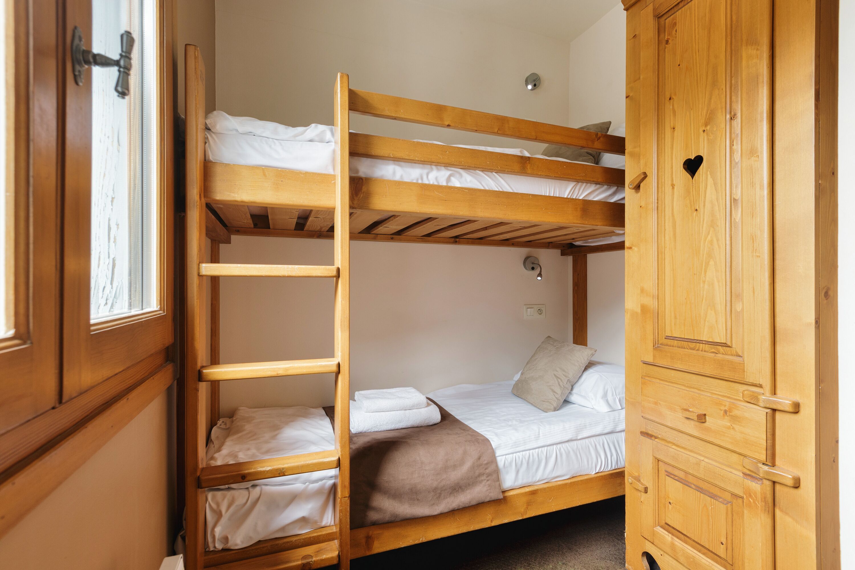 A bunk bed with a ladder, a wooden wardrobe, and a window with a door.