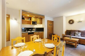 A dining area with a wooden table set for four, a kitchen with wooden cabinets and a microwave, and a brown sofa with a cushion. - Vallorcine Buet 32 ski in / ski out, Vallorcine (Argentiere), France (Vallorcine (Argentiere))