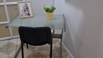 Uma mesa com tampo de vidro, uma moldura com fotografia e um vaso com planta.