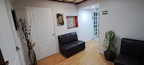 A reception area with a black leather sofa, a potted plant, and a door with a framed picture. - Habitaciones Narvarte Del Valle (Mexico City)