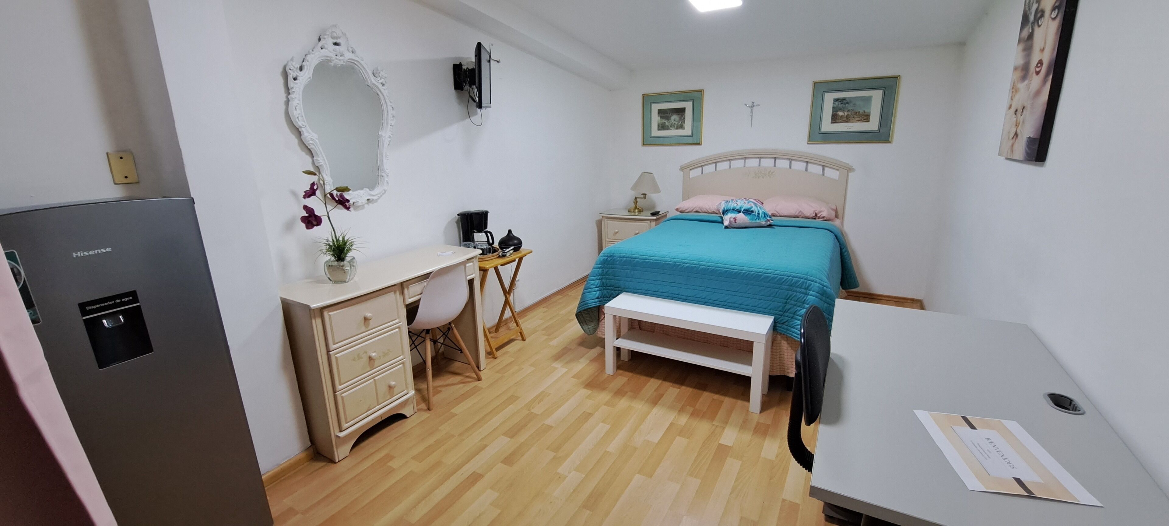 A bedroom with a bed, bedside table, desk, chair, and a refrigerator.