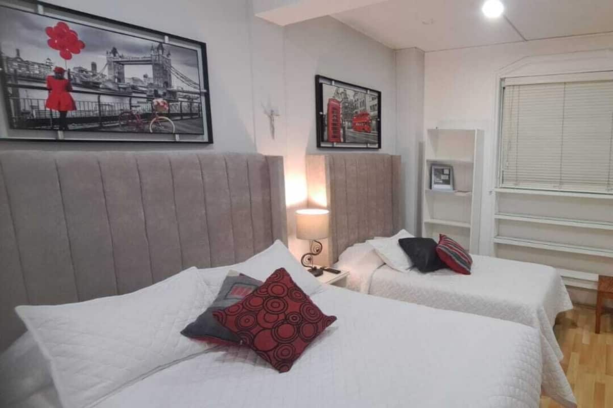 A hotel room with two beds, a window with blinds, a door, and artwork on the walls.
