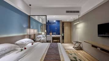 Une chambre d’hôtel moderne dotée d’un grand lit, d’un bureau, d’un miroir, d’une télévision et d’une salle de bain visible à travers une paroi en verre.