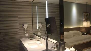 A modern hotel room with a large bed, a bedside table with a coffee maker, a mirror, and a wall-mounted phone.