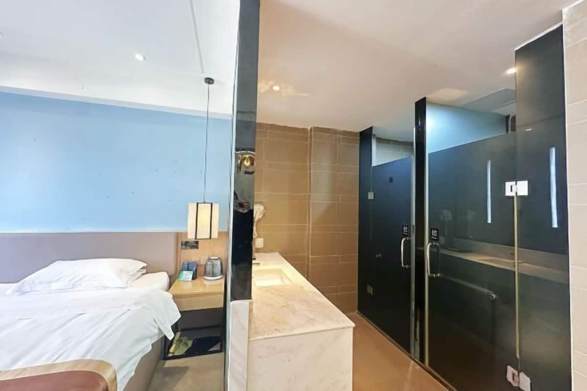 A modern hotel room with a bed, bedside table, and a glass-enclosed shower area.