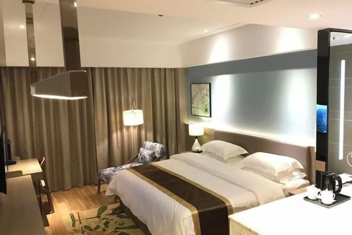A hotel room with a bed, bedside tables, a desk, a chair, a lamp, a painting on the wall, and a television.