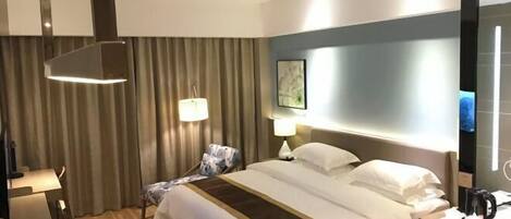 Habitación de hotel con cama, mesitas de noche, escritorio, silla, lámpara, un cuadro en la pared y televisor.