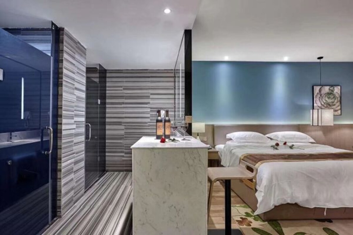 A modern hotel room with a bed, bedside table, and a shower area.