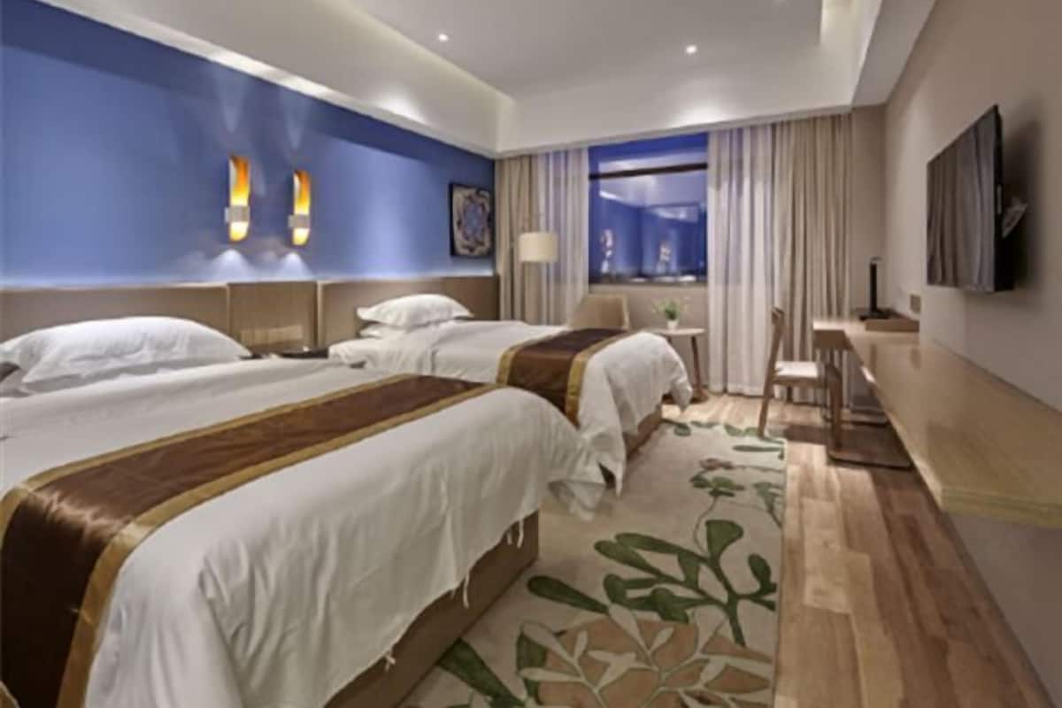 A hotel room with two beds, a desk, a chair, a TV, and a window with curtains.