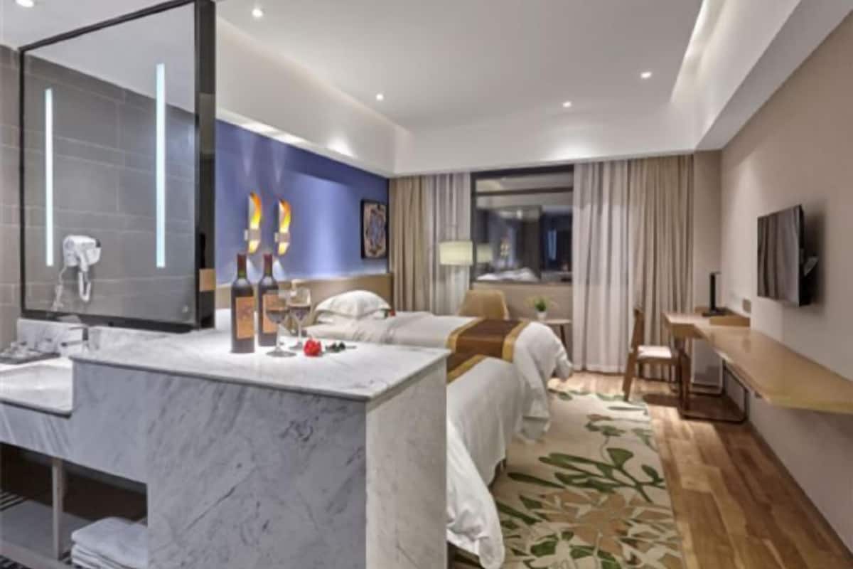 A hotel room with a marble bathroom, a bed with white linens, a desk, and a television.