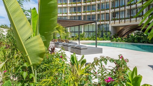 Un hotel con piscina, mobiliario exterior y abundante vegetación.