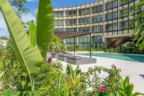 Un hotel con piscina, mobiliario exterior y abundante vegetación.