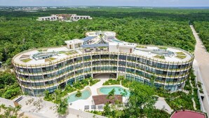 Un hotel moderno con diseño circular, varios pisos y un patio central con piscinas.