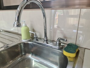 Een roestvrijstalen spoelbak met een moderne kraan, een fles afwasmiddel en een spons.