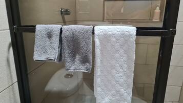 A glass-enclosed shower stall with a toilet and a towel rack holding three towels.