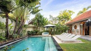 A swimming pool with lounge chairs and a small seating area, surrounded by tropical plants and a building with a tiled roof. - Modern & Luxury 4BR Villa in Seminyak w/ Fast Wifi (Badung)