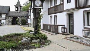A building with a clock tower, stone archway, and a small garden area. - Schuss Mountain. 2 bedroom, 1.5 bath Sleeps 6. Pool Dog Friendly boat parking (Mancelona)