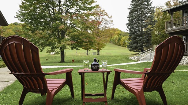 Two wooden Adirondack chairs with a small table between them, featuring two bottles and a coffee mug. - Schuss Mountain. 2 bedroom, 1.5 bath Sleeps 6. Pool Dog Friendly boat parking (Mancelona)