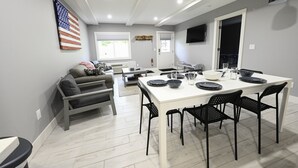 A modern living room with a white dining table set for four, black chairs, a gray sofa, and a large American flag on the wall. - Schuss Mountain. 2 bedroom, 1.5 bath Sleeps 6. Pool Dog Friendly boat parking (Mancelona)