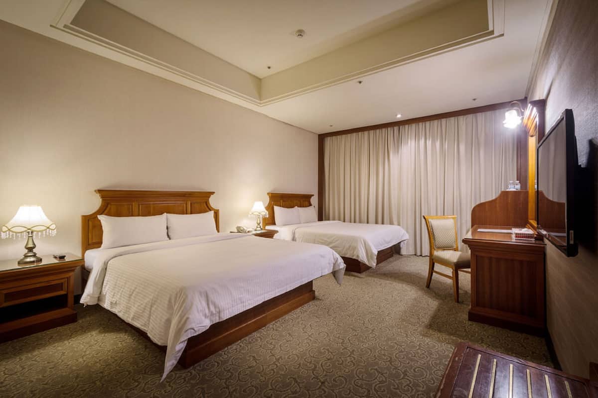 A hotel room with two beds, a desk, a chair, a TV, and a mirror.
