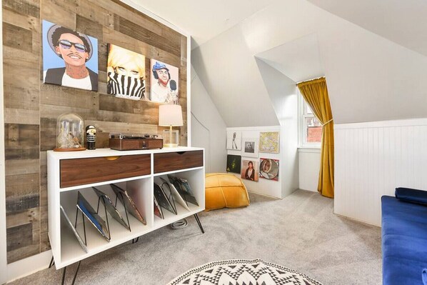 A cozy attic bedroom with a sloped ceiling, a white console table with a record player, a yellow bean bag, and a patterned rug. - ★ HostWise Stays ★ 4 Blocks From UPMC Children's (Pittsburgh)