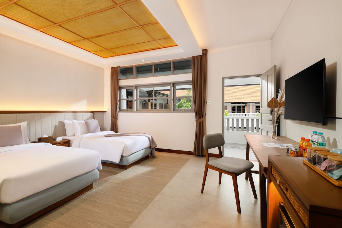 A hotel room with two beds, a desk with a chair, a television, and a large window.