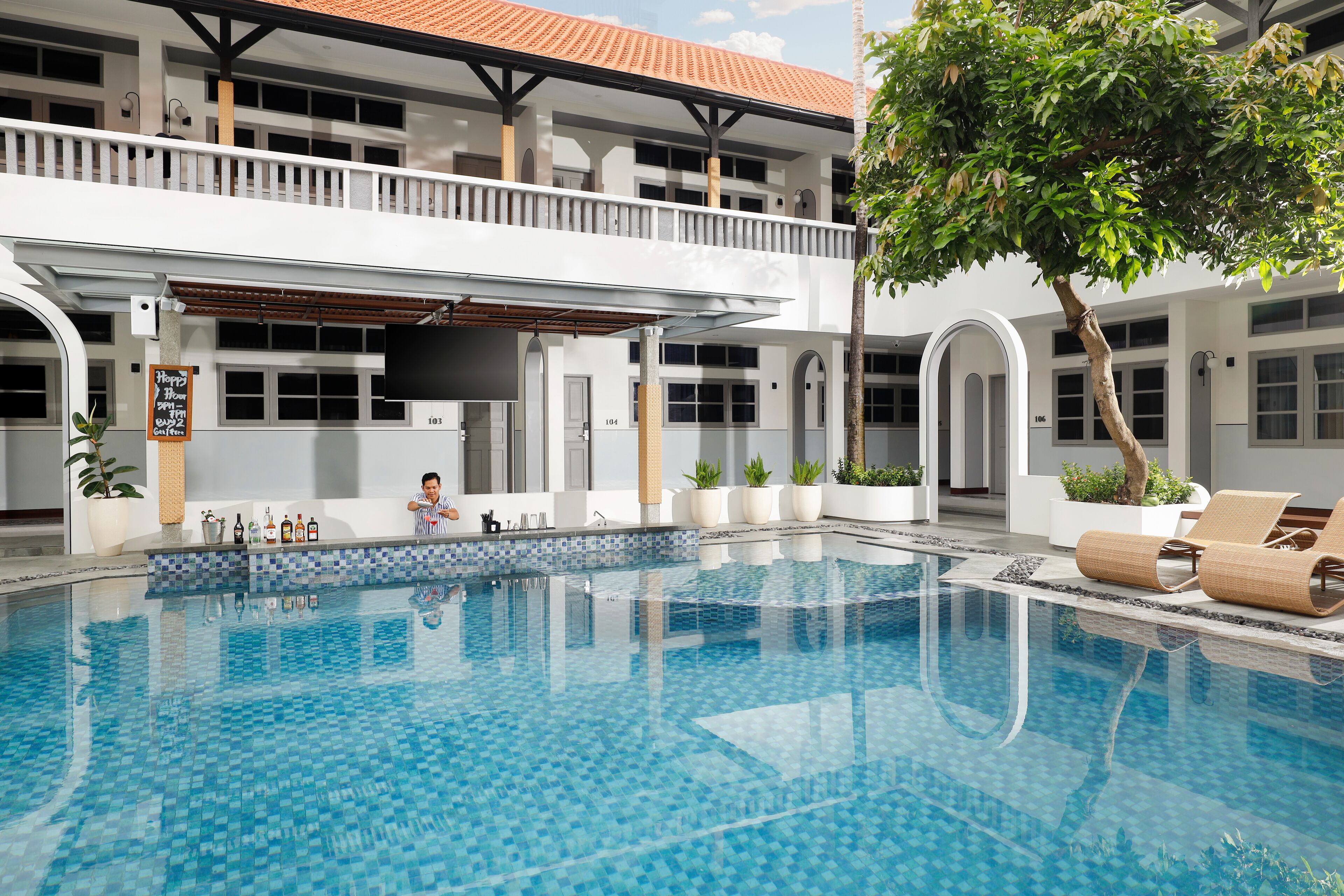 A swimming pool with a tiled deck, surrounded by a building with multiple balconies and potted plants.