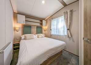 A bedroom with a bed, bedside lamps, a window with curtains, and a radiator.