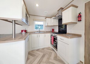 A compact kitchen with white cabinets, a stainless steel range hood, a red toaster, and a window with blinds.