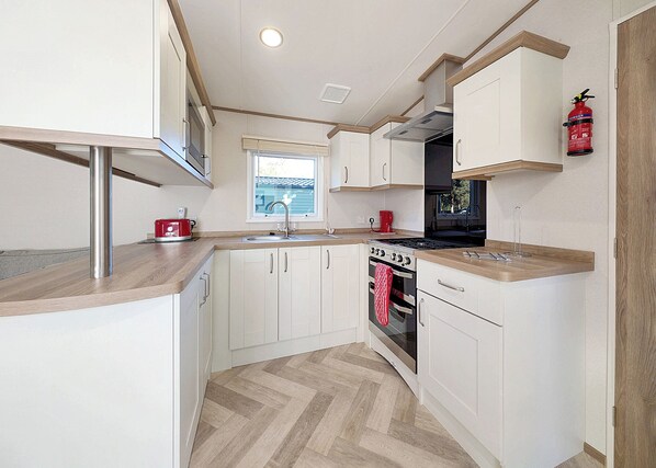 Una cocina compacta con armarios blancos, una campana extractora de acero inoxidable, un tostador rojo y una ventana con persianas.