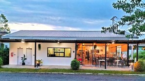 A building with a metal roof, a reception area with a window, and an open dining area with tables and chairs. - Blue Moon Boutique Resort (Sichon)