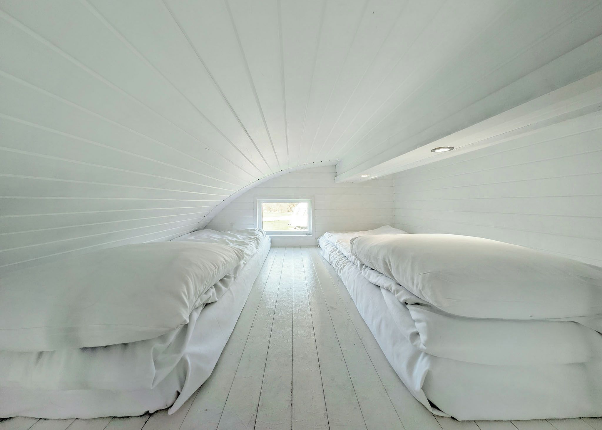 Habitación con dos camas, piso de madera y techo inclinado con tragaluz.