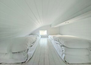 Une chambre avec deux lits, un plancher en bois et un plafond en pente doté d’un puits de lumière.
