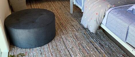A dormitory room with bunk beds, a round ottoman, a small round table with a bowl, and a potted plant.