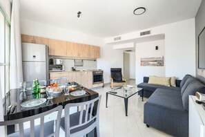 A modern kitchen with wooden cabinets, a dining table with chairs, a sofa, and a painting on the wall.