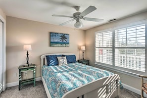 A bedroom with a bed, two bedside lamps, a ceiling fan, a window with blinds, and a painting on the wall. - Breezy Darien Condo w/ Tranquil Marsh Views! (Darien)