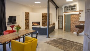 A modern living room with a fireplace, a dining area with a wooden table and yellow chairs, and a brick wall.