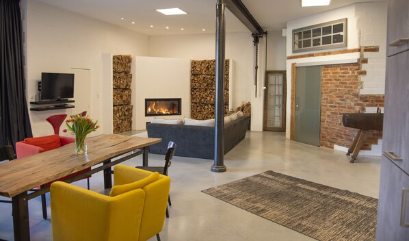 A modern living room with a fireplace, a dining area with a wooden table and yellow chairs, and a brick wall. - Vacation apartment Höttingen - Adults Only - near Brombachsee (Höttingen)