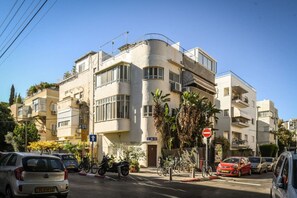 Un immeuble résidentiel à plusieurs étages, doté de balcons, avec des voitures et des vélos garés devant.