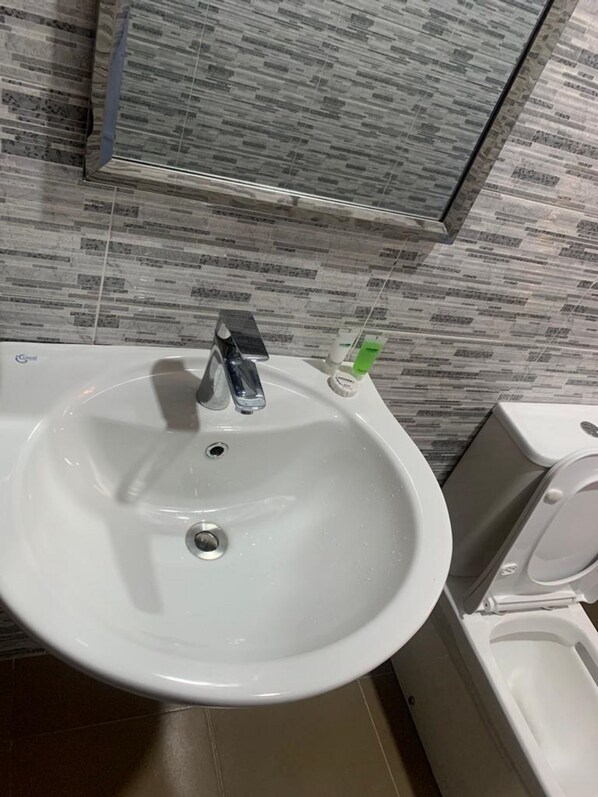 Une salle de bain avec un lavabo blanc, un miroir au-dessus et des toilettes sur la droite.