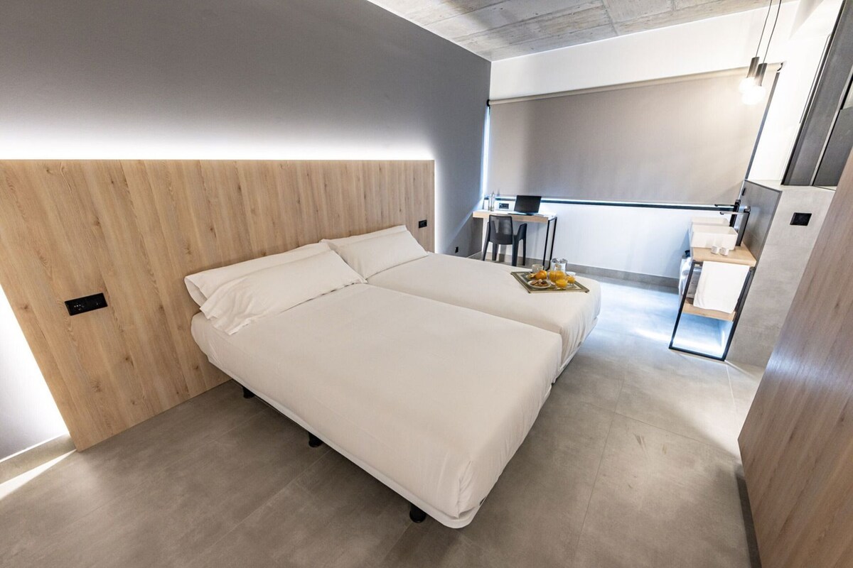 Quarto de hotel moderno com uma cama grande, uma escrivaninha e uma pequena cozinha equipada.