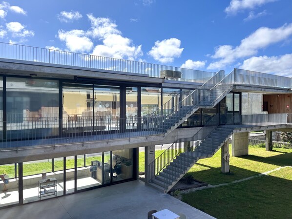 A modern building with a glass facade, outdoor seating area, and a staircase leading to an upper level. - Hotel VIDA Devalar do Mar (Camarinas)