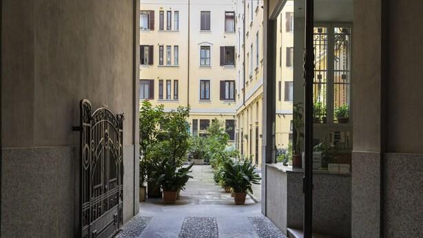 A narrow corridor with a stone floor, flanked by buildings with balconies and potted plants. - notaMi - Cosy Home - Porta Romana MM3 (Milan)