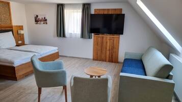 Ein modernes Hotelzimmer mit einem Bett, zwei Sesseln, einem Sofa, einem kleinen Tisch, einem Fernseher und einem Fenster mit Vorhängen.