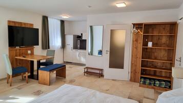 A hotel room with a bed, a desk with a chair, a television, a kitchenette, and a wardrobe.