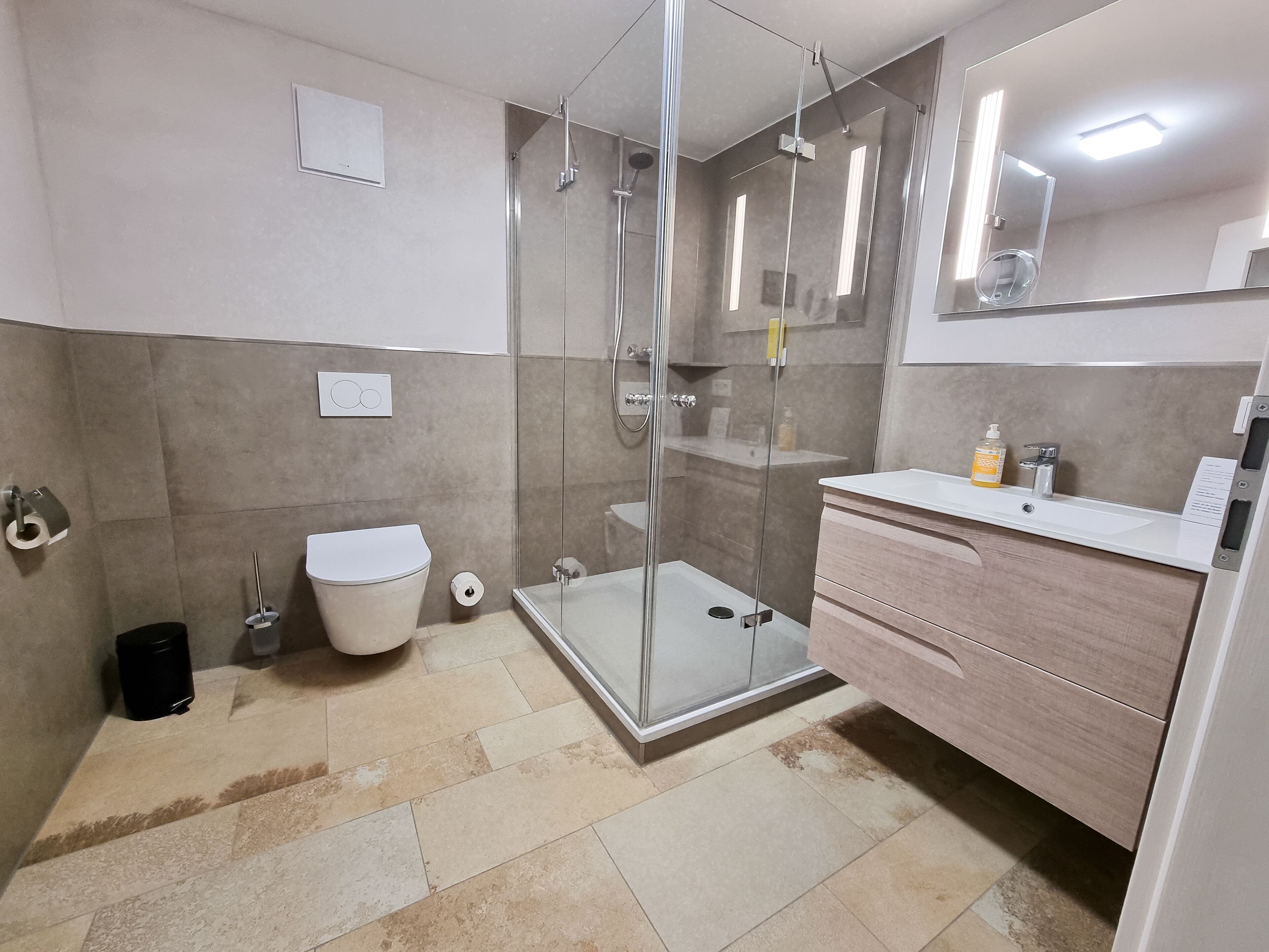 Un baño moderno con cabina de ducha de vidrio, inodoro blanco y tocador con espejo.