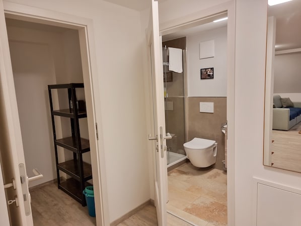 A bathroom with a toilet, shower, and a glass-enclosed walk-in closet with shelves. - Gästehaus Mönchswald (Muhr am See)